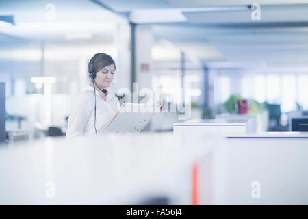 businesswoman wearing headset and reading document in cubicle, Freiburg Im Breisgau, Baden-Württemberg, Germany Stock Photo
