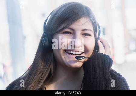 Portrait of a young woman smiling talking on headset, Freiburg im Breisgau, Baden-Württemberg, Germany Stock Photo