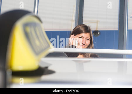 Young woman talking on mobile phone behind a taxi, Freiburg im Breisgau, Baden-Württemberg, Germany Stock Photo