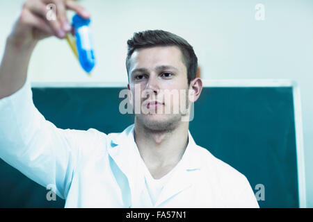 Young male chemistry teacher closely observing the solutions in classroom, Freiburg Im Breisgau, Baden-Württemberg, Germany Stock Photo