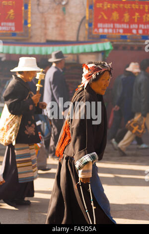 Mature female Tibetan pilgrim wearing traditional brown Tibetan garb, holding beads, walking or circumambulating around Jokhang Stock Photo