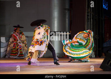 Female dancer wearing colorful green dress, bending body sideways dancing with male partner in cape during a Mexican dance Stock Photo