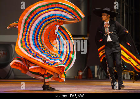 Man wearing traditional clothes dancing a Mexican hat dance with woman flailing her orange dress in pattern at a folk show at a Stock Photo