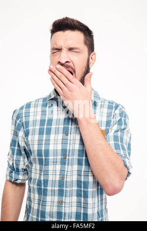Tired exhausted bearded young man in checkered shirt standing and yawning Stock Photo