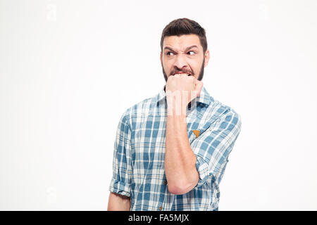 Angry irritated aggressive young bearded man in plaid shirt biting his fist over white background Stock Photo