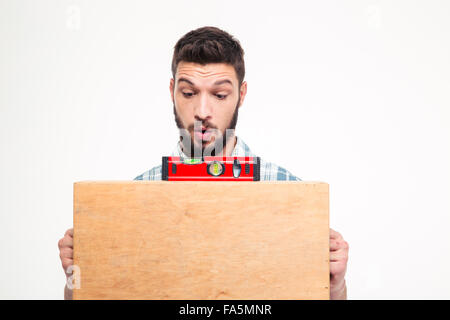Amusing concentrated young bearded man using bubble level on wooden surface over white background Stock Photo