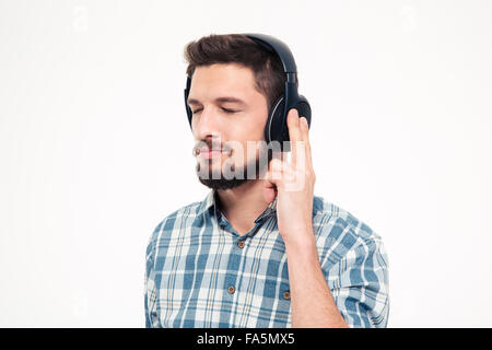 Relaxed thoughtful young man with beard in checkered shirt listening to music using headphones with eyes closed over white backg Stock Photo