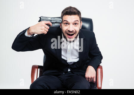 Crazy hysterical bearded young businessman sitting on black office chair and put gun to his temple over white background Stock Photo