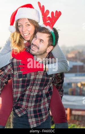 Couple in love piggyback riding outdoors with Christmas hats Stock Photo