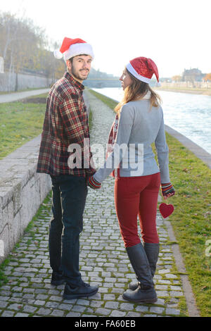 Couple in love walking outdoors holding hands with Christmas hats Stock Photo