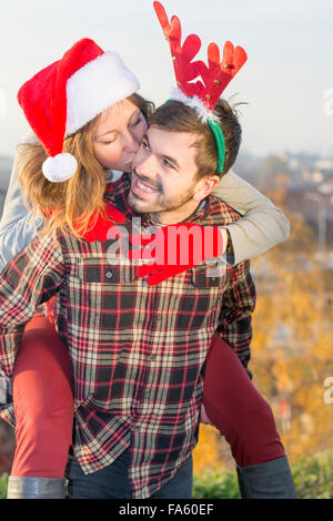 Couple in love piggyback riding outdoors with Christmas hats Stock Photo