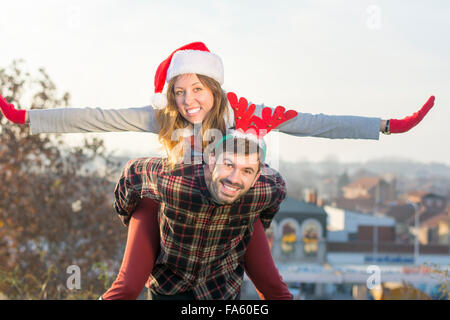 Couple in love piggyback riding outdoors with Christmas hats Stock Photo