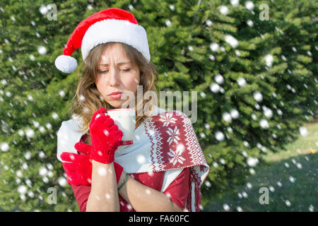 Beautiful Santa Claus girl having cup of tee outdoors in front big fir tree Stock Photo