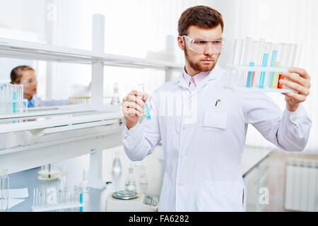 Young chemist looking at flasks with liquid chemical substances