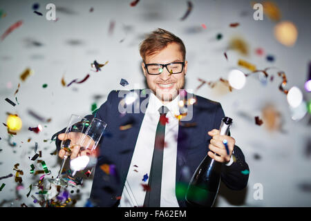 Happy businessman with bottle of champagne and two glasses standing under falling confetti Stock Photo