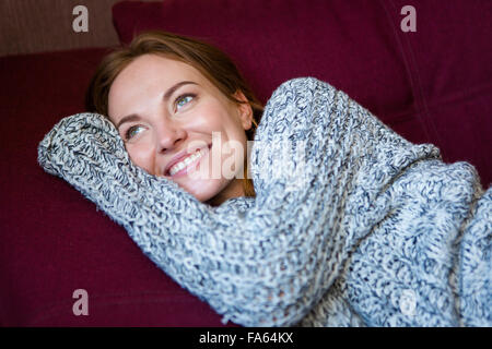 Portrait of beautiful cheerful young woman in grey knitted sweater lying on couch Stock Photo