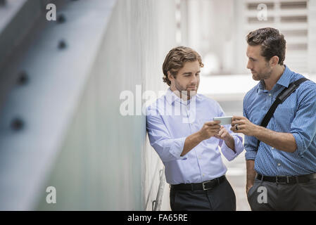 Two businessmen standing in an urban street, using smart phones. Stock Photo