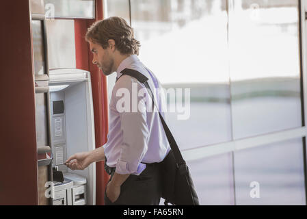 A man with a laptop bag using an ATM, a cash machine on a city street. Stock Photo