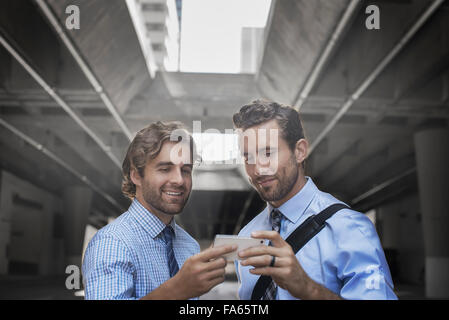 Two men in shirts and ties taking a selfie with a smart phone, with an urban walkway and tall buildings in the background. Stock Photo