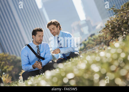 Two men in shirts and ties in a park in the city holding their smart phones. Stock Photo