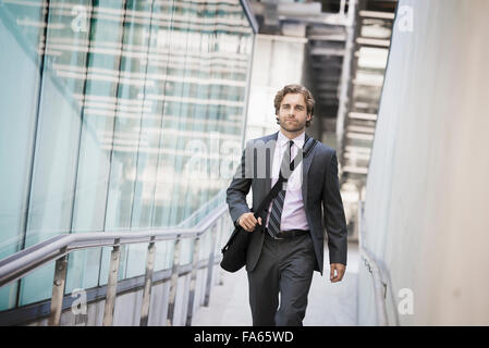 A man carrying a computer bag with a strap on a city walkway. Stock Photo
