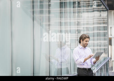 A man standing outside a building with large glass exterior panels, using a digital tablet. Stock Photo