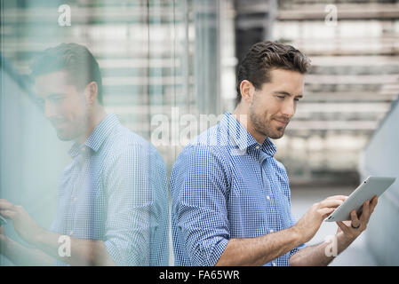 A man standing outside a building with large glass exterior panels, using a digital tablet. Stock Photo