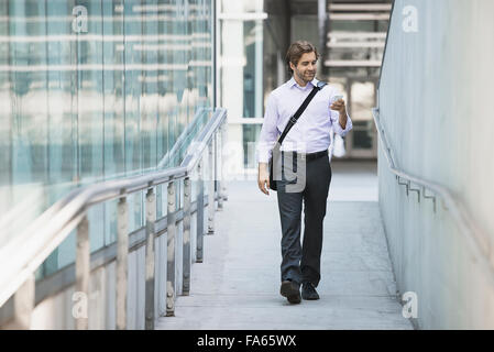 A man carrying a computer bag with a strap across his chest on along a city walkway. Stock Photo