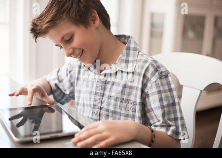 A boy seated at a table using a digital tablet, hand on the touch screen. Stock Photo