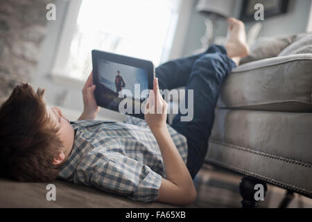 A boy lying on his front on the floor, looking at a digital tablet. Stock Photo