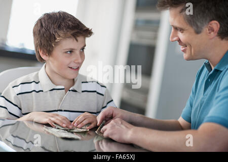 A man and a boy seated at a table, counting and handling cash. Stock Photo
