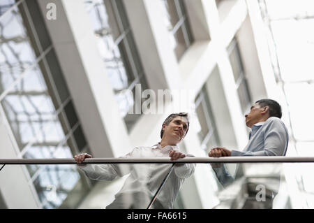 Two men, business colleagues, standing by a railing in an atrium or courtyard, talking. Stock Photo
