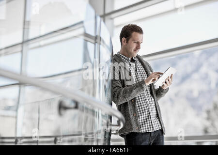 A man standing leaning against a glass panel, using a digital tablet. Stock Photo