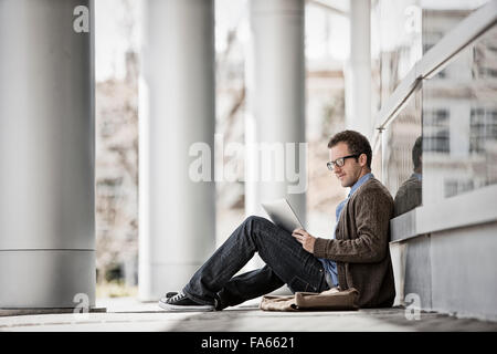 A man sitting outside a building on steps using a digital tablet. Stock Photo