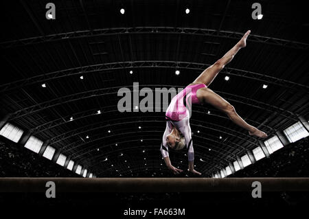 A young woman gymnast performing on the beam, balancing on her hands on a narrow piece of apparatus. Stock Photo
