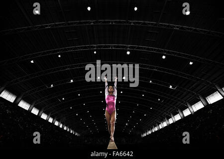 A young woman gymnast performing on the beam, balancing on a narrow piece of apparatus. Stock Photo
