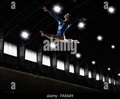 A female gymnast, a young woman performing a floor routine, in mid air with legs and arms outstretched and back bent. Stock Photo