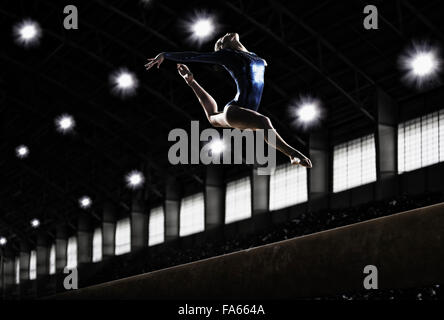 A female gymnast, a young woman performing a floor routine, in mid air with legs and arms outstretched and back bent. Stock Photo