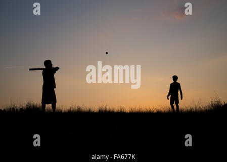 Silhouette of man and teenage boy playing baseball Stock Photo