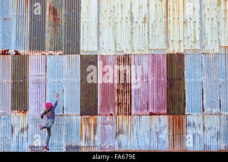 Girl jumping in front of a colorful corrugated metal wall, Kalgoorlie, Western Australia Stock Photo