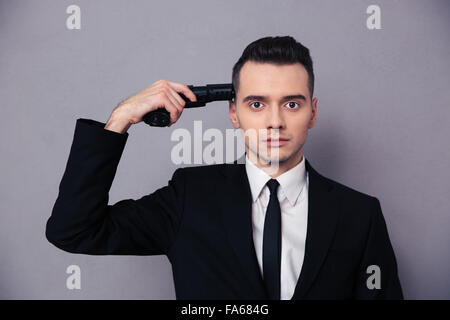 Portrait of a young businessman standing with gun over head on gray background Stock Photo