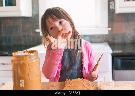 Girl making peanut butter sandwich, licking fingers Stock Photo