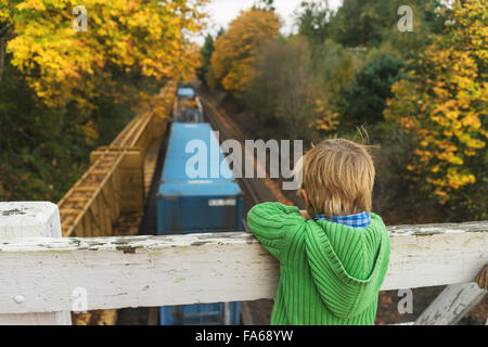 Boy standing on bridge looking at train below Stock Photo