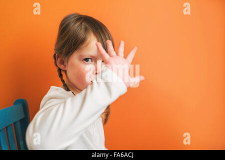 Girl sitting on a chair pouting and holding her hand in front of her face Stock Photo