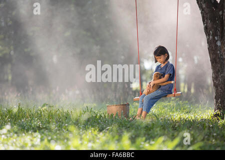 Girl sitting on a swing with dog on her lap
