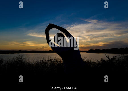 Man sitting by lake doing yoga exercise at sunset Stock Photo