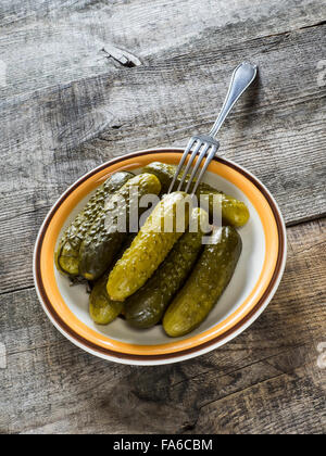 Pickled green gherkins with a fork in a bowl on a wooden table Stock Photo