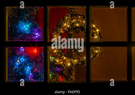 Illuminated wreath and Christmas tree lights through a lodge window. Stock Photo