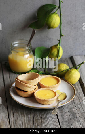 Lemon curd tarts and baked pastry on a plate and a jar of lemon curd and fresh lemon on background Stock Photo