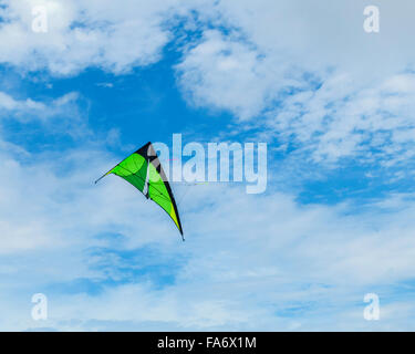 A black and green dart-shaped kite soaring against a sky of blue with clouds. Stock Photo